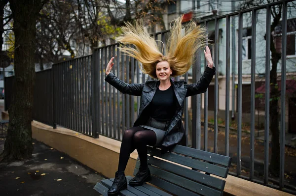 Blonde fashionable girl in long black leather coat posed on benc — Stock Photo, Image