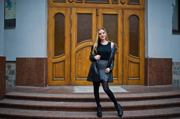 Blondes modisches Mädchen im langen schwarzen Ledermantel posierte gegen — Stockfoto