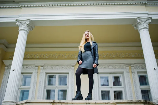 Blondes modisches Mädchen im langen schwarzen Ledermantel posierte gegen — Stockfoto