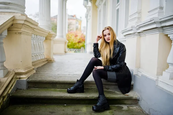 Blondes modisches Mädchen im langen schwarzen Ledermantel posierte gegen — Stockfoto