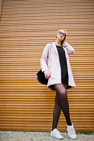 Blonde girl at glasses and pink coat against shutters. — Stock Photo, Image