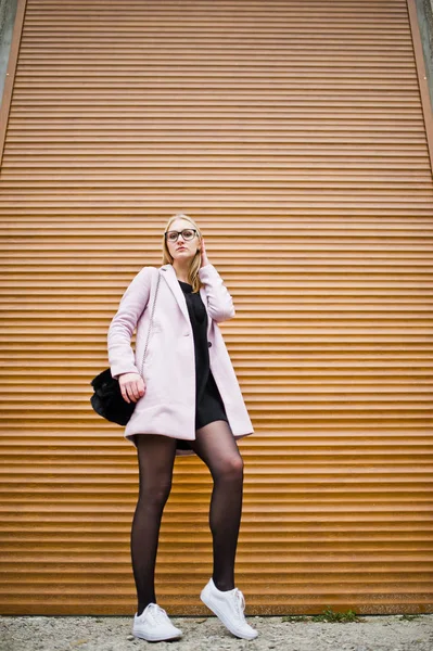 Blond flicka på glasögon och rosa kappa mot fönsterluckor. — Stockfoto