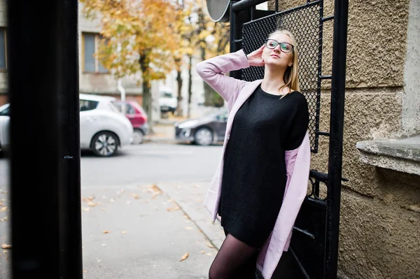 Blond meisje op bril en roze jas, zwarte tuniek gesteld op stree — Stockfoto