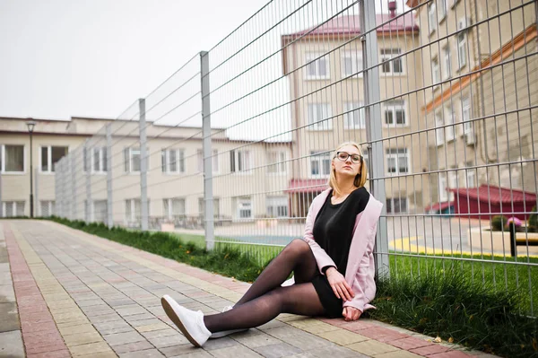 Blondes Mädchen mit Brille und rosa Mantel, schwarzer Tunika im Sitzen — Stockfoto