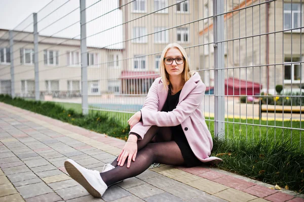 Chica rubia en gafas y abrigo rosa, túnica negro sentado de nuevo — Foto de Stock