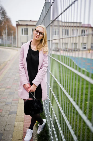 Menina loira em óculos e casaco rosa, túnica preta e bolsa po — Fotografia de Stock