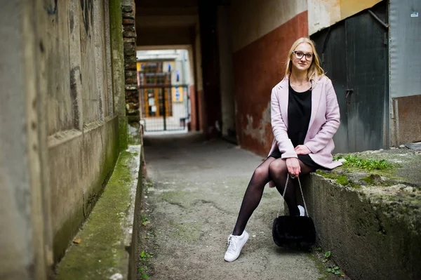 Blond flicka på glasögon och rosa kappa, svart tunika och handväska po — Stockfoto