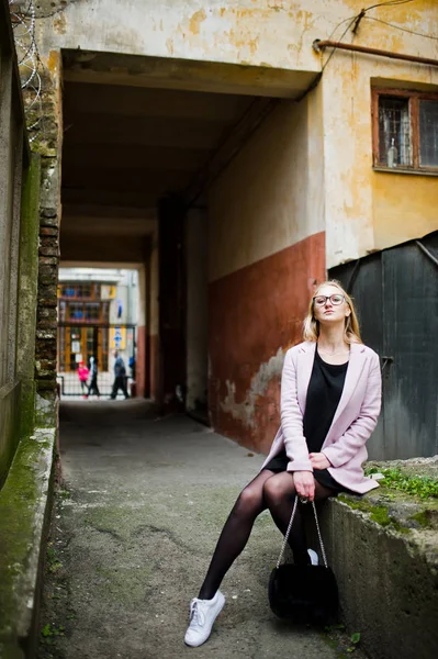 Blondes Mädchen mit Brille und rosa Mantel, schwarzer Tunika und Handtasche — Stockfoto