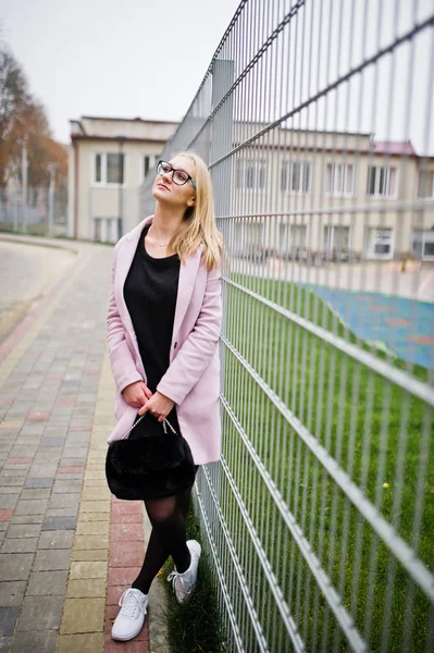 Blondes Mädchen mit Brille und rosa Mantel, schwarzer Tunika und Handtasche — Stockfoto