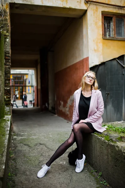 Blondes Mädchen mit Brille und rosa Mantel, schwarzer Tunika und Handtasche — Stockfoto