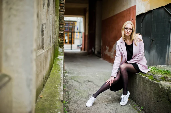 Blond flicka på glasögon och rosa kappa, svart tunika och handväska po — Stockfoto