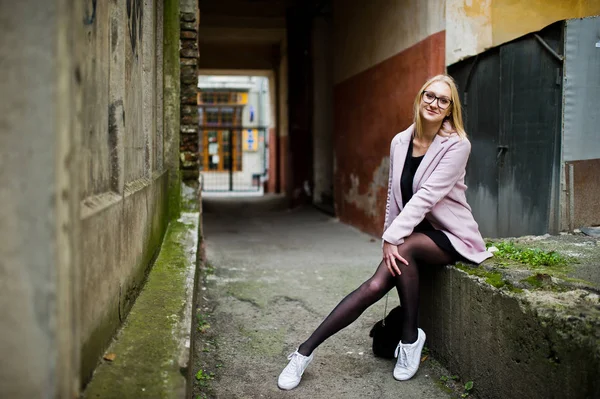 Blond flicka på glasögon och rosa kappa, svart tunika och handväska po — Stockfoto