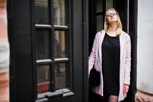 Chica rubia en gafas y abrigo rosa, túnica negra posó contra — Foto de Stock