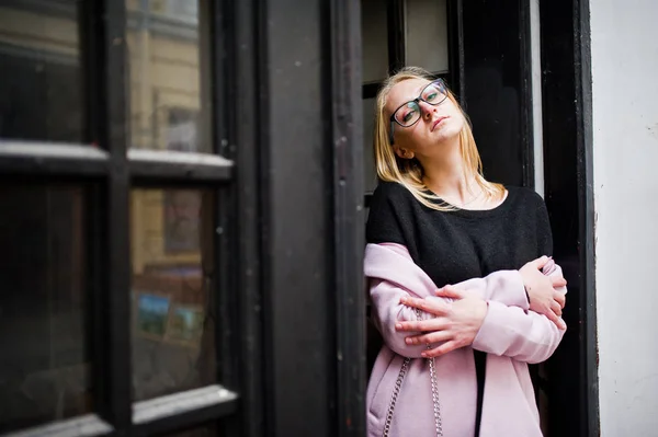 Chica rubia en gafas y abrigo rosa, túnica negra posó contra — Foto de Stock