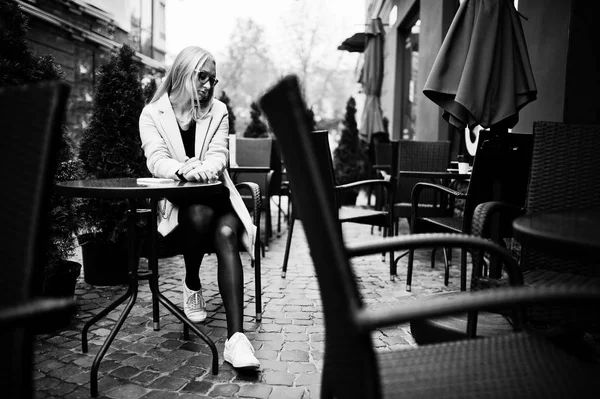 Fille blonde à lunettes et manteau rose, tunique noire assise à l'onglet — Photo