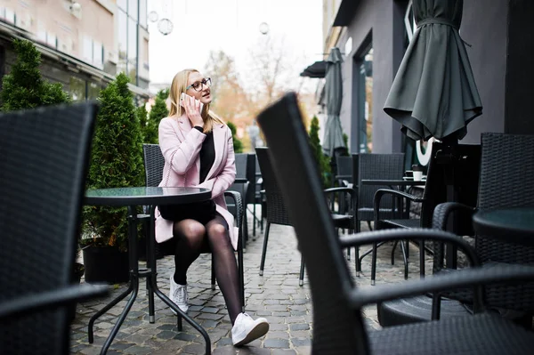 Blonde girl at glasses and pink coat, black tunic sitting at tab — Stock Photo, Image