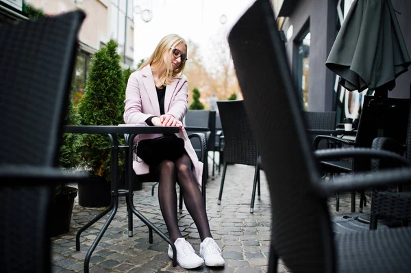 Ragazza bionda a occhiali e cappotto rosa, tunica nera seduta al tab — Foto Stock