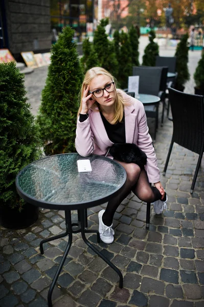 Blond flicka på glasögon och rosa kappa, svart tunika sitter på fliken — Stockfoto