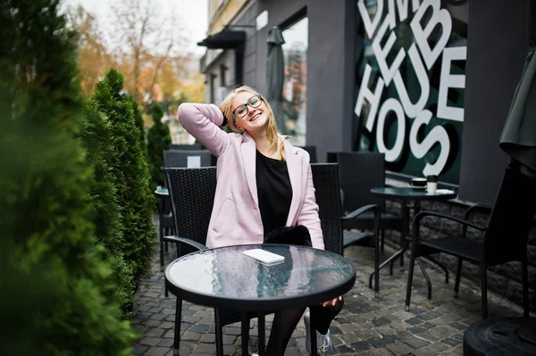 Blond meisje op glazen en roze jas, black tuniek zit op tabblad — Stockfoto