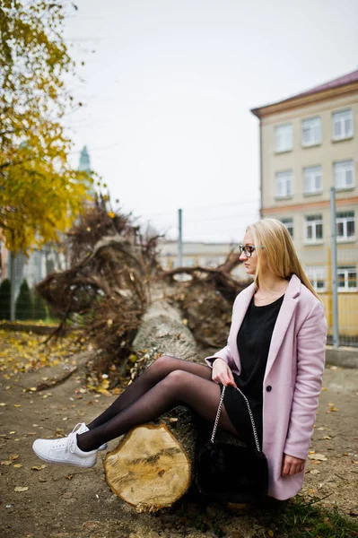 Blondes Mädchen mit Brille und rosa Mantel, schwarzer Tunika sitzend auf Schnitt — Stockfoto