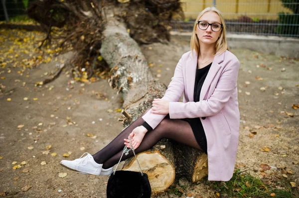 Blondes Mädchen mit Brille und rosa Mantel, schwarzer Tunika sitzend auf Schnitt — Stockfoto