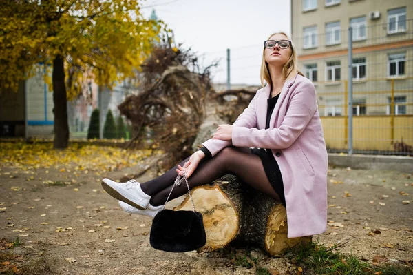 Fille blonde à lunettes et manteau rose, tunique noire assise sur la coupe — Photo