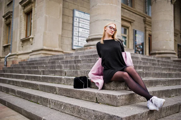 Blondes Mädchen mit Brille und rosa Mantel mit Handtasche auf dem Schoß — Stockfoto