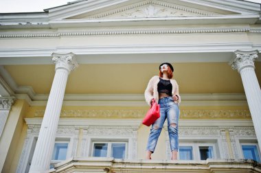 Kırmızı saçlı kız gözlük ve şapka kırmızı el çantası ile v poz verdi.