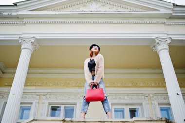 Kırmızı saçlı kız gözlük ve şapka kırmızı el çantası ile v poz verdi.