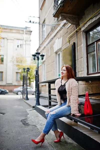 Červené vlasy dívka s červenou kabelku představují na ulici města. — Stock fotografie