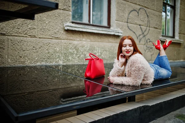 Fille aux cheveux rouges avec sac à main rouge posé à la rue de la ville . — Photo