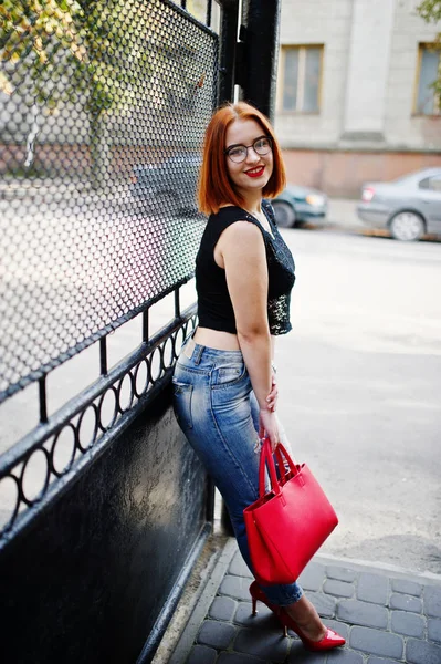 Chica pelirroja en gafas con bolso rojo posado en la calle de c —  Fotos de Stock