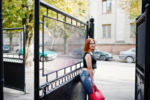 Chica pelirroja en gafas con bolso rojo posado en la calle de c — Foto de Stock