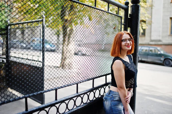 Chica pelirroja en gafas con bolso rojo posado en la calle de c —  Fotos de Stock