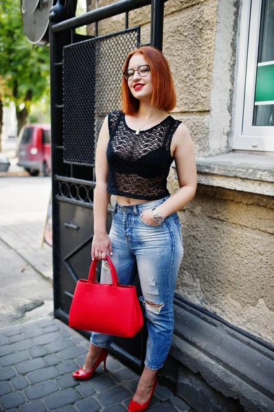 Chica pelirroja en gafas con bolso rojo posado en la calle de c —  Fotos de Stock