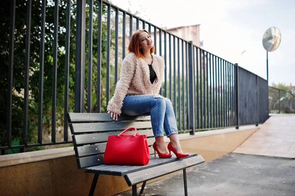 Рыжая девушка с красной сумочкой позировала на скамейке . — стоковое фото