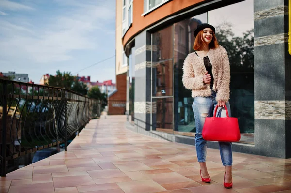 Chica pelirroja en sombrero con bolso rojo posado cerca de la casa moderna —  Fotos de Stock