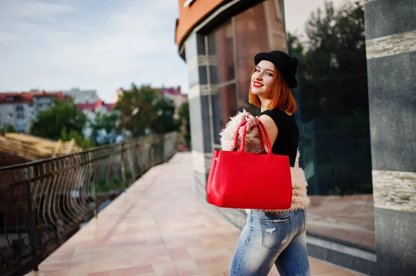 Chica pelirroja en sombrero con bolso rojo posado cerca de la casa moderna —  Fotos de Stock