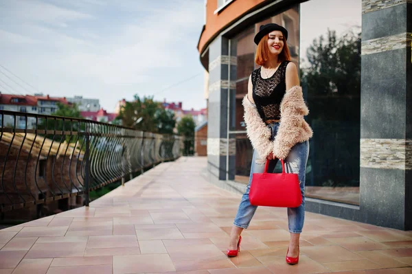 Chica pelirroja en sombrero con bolso rojo posado cerca de la casa moderna —  Fotos de Stock