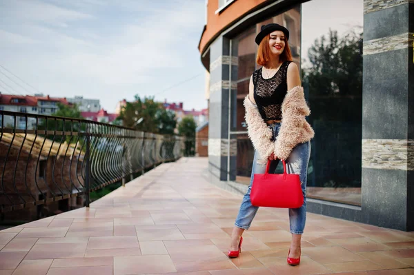 Fille aux cheveux rouges dans un chapeau avec sac à main rouge posé près de la maison moderne — Photo