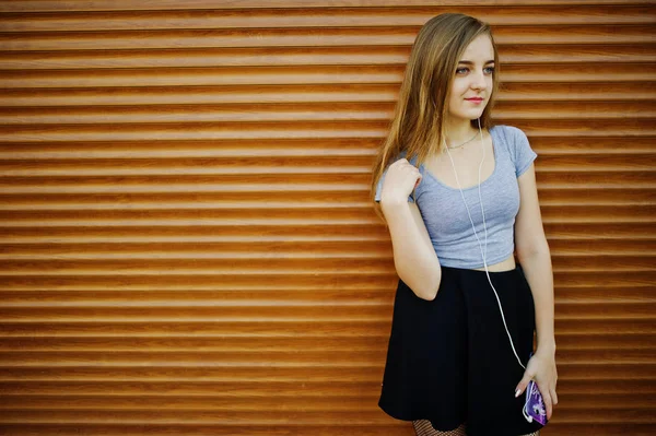 Chica rubia joven en falda negra escuchando música de auriculares — Foto de Stock