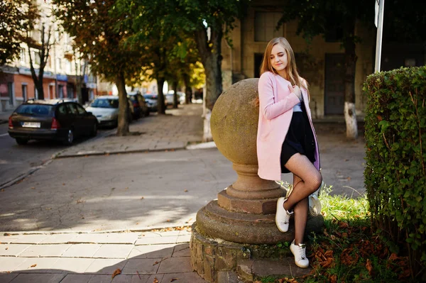 Giovane ragazza bionda in gonna nera e cappotto rosa posato a soleggiata da — Foto Stock