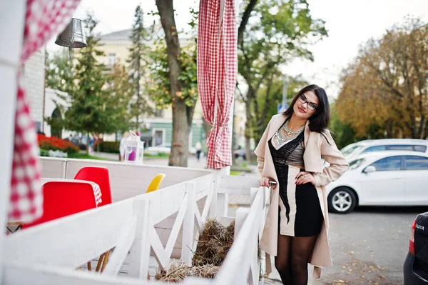 Black hair sexy woman in glasses and coat posed on street. — Stock Photo, Image