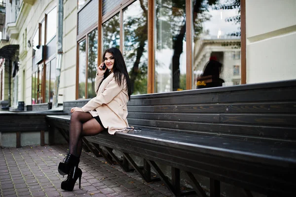 Cheveux noirs femme sexy en lunettes et manteau assis sur le banc et s — Photo