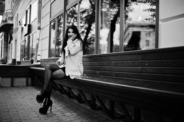 Μαύρα μαλλιά σέξι γυναίκα γυαλιά και παλτό κάθεται σε παγκάκι. — Φωτογραφία Αρχείου