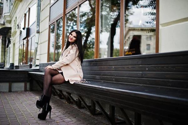 Μαύρα μαλλιά σέξι γυναίκα γυαλιά και παλτό κάθεται σε παγκάκι. — Φωτογραφία Αρχείου