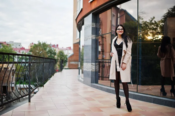 Black hair sexy woman in glasses and coat posed against building — Stock Photo, Image