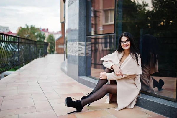 Preto cabelo sexy mulher no óculos e casaco posado contra a construção — Fotografia de Stock