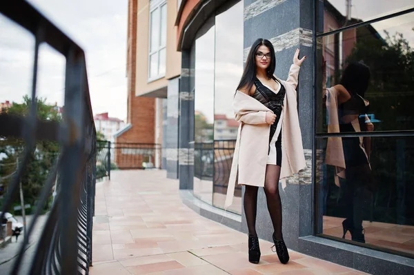 Black hair sexy woman in glasses and coat posed against building — Stock Photo, Image