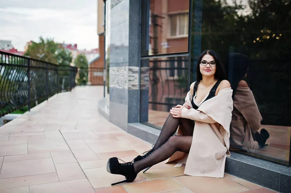 Preto cabelo sexy mulher no óculos e casaco posado contra a construção — Fotografia de Stock